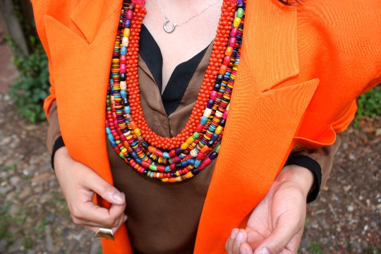 a layered necklace worn with an orange vintage 1980s blazer