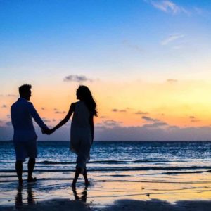 Free Man and Woman Holding Hands Walking on Seashore during Sunrise Stock Photo